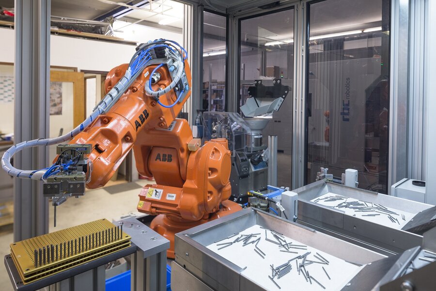 Orangefarbener Industrieroboter der rbc robotics FXA Load A bei der automatisierten Werkstückhandhabung in einer Schutzzelle.